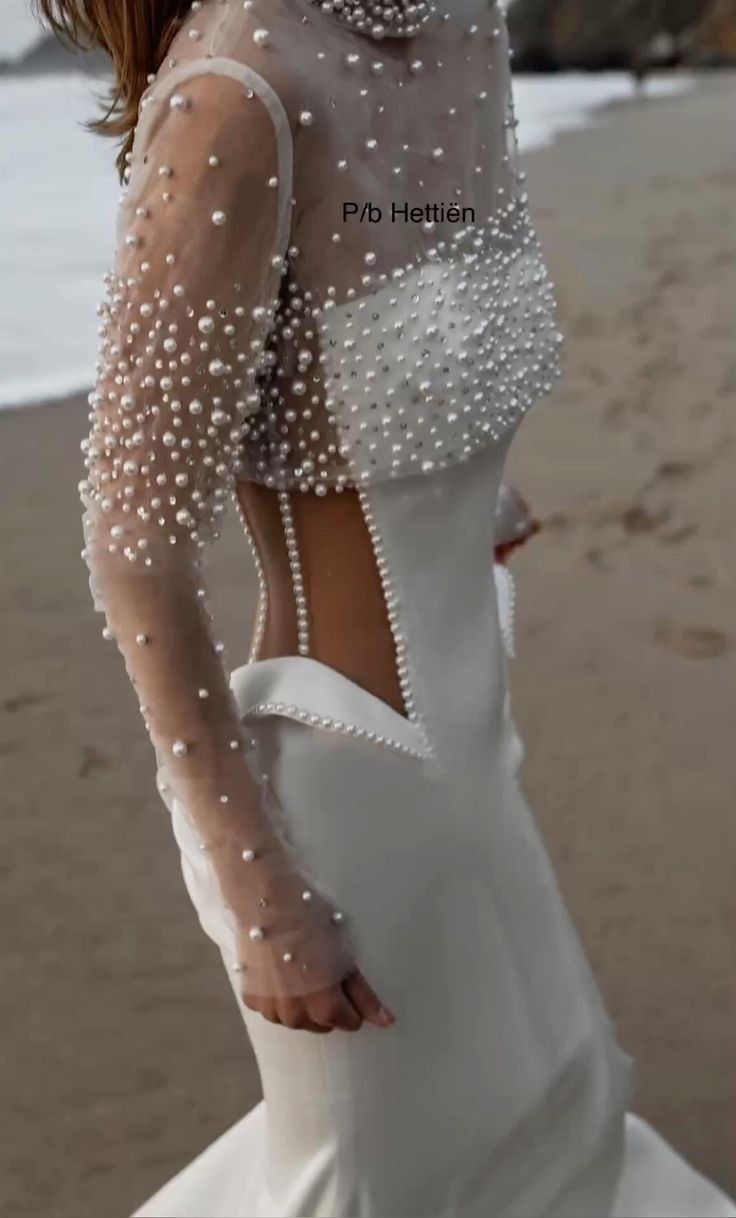 a woman in a white dress standing on the beach with her back to the camera