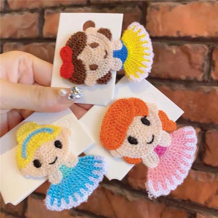 crocheted little angel broochies are being held in front of a brick wall