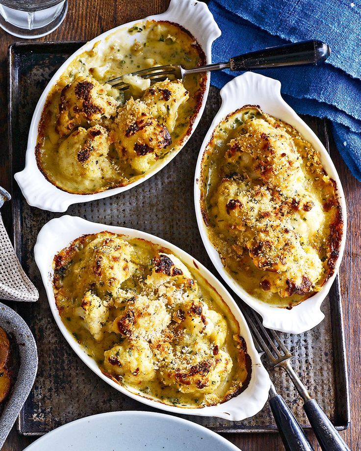 three casserole dishes with cheese and meat in them on a tray next to silverware