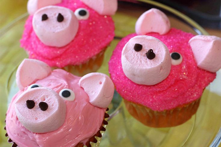 three cupcakes with pink frosting and pig faces on them sitting on a glass plate