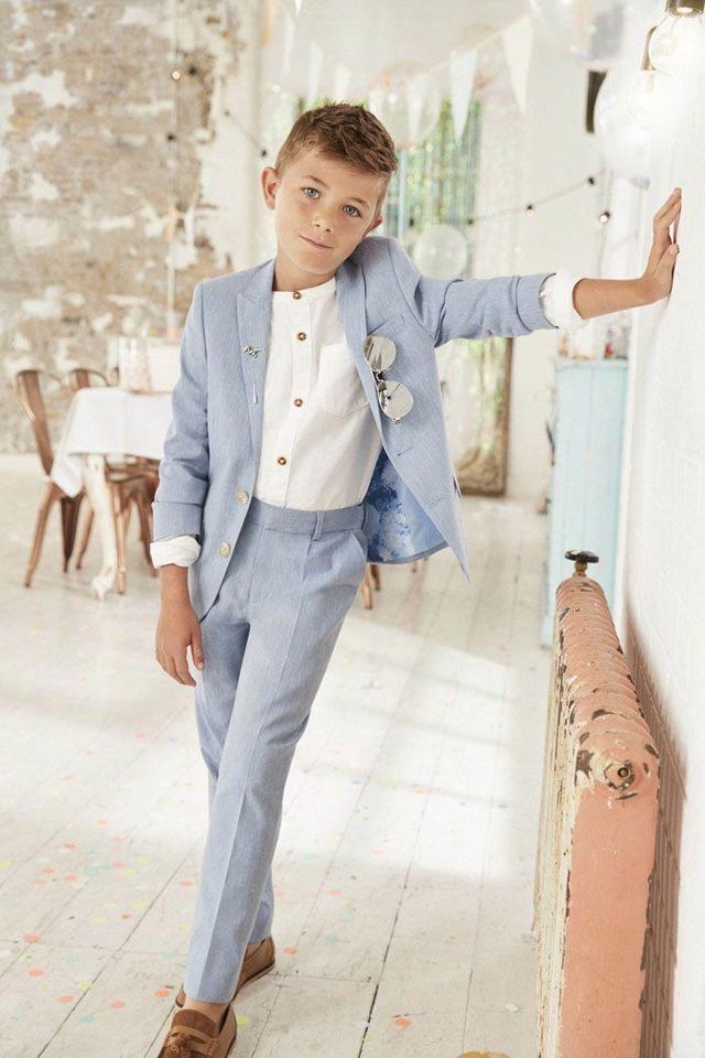 a young boy in a blue suit leaning against a wall