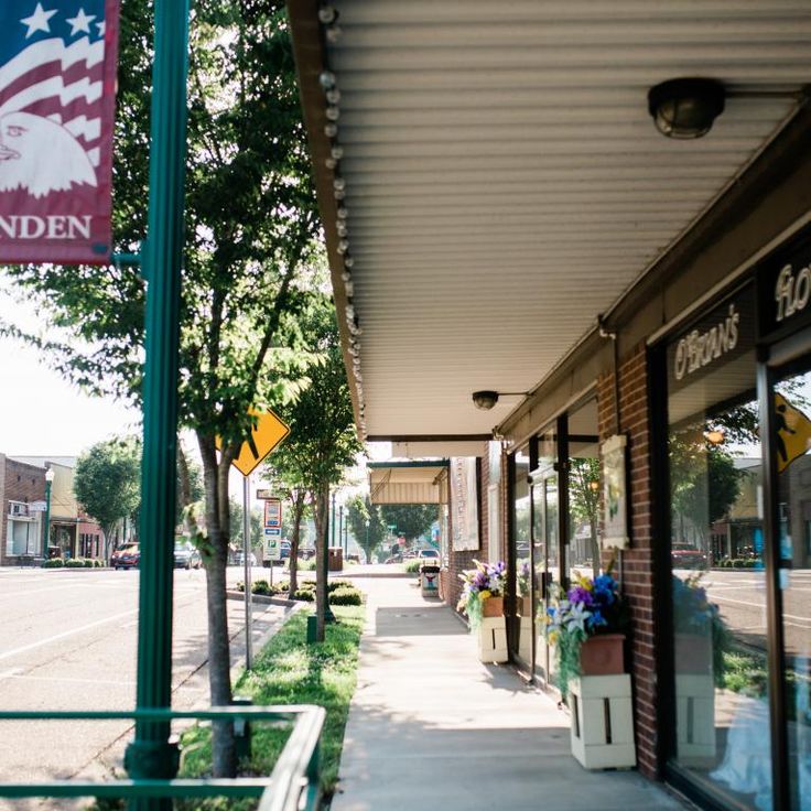 an american flag hanging from the side of a building next to a sidewalk with potted plants