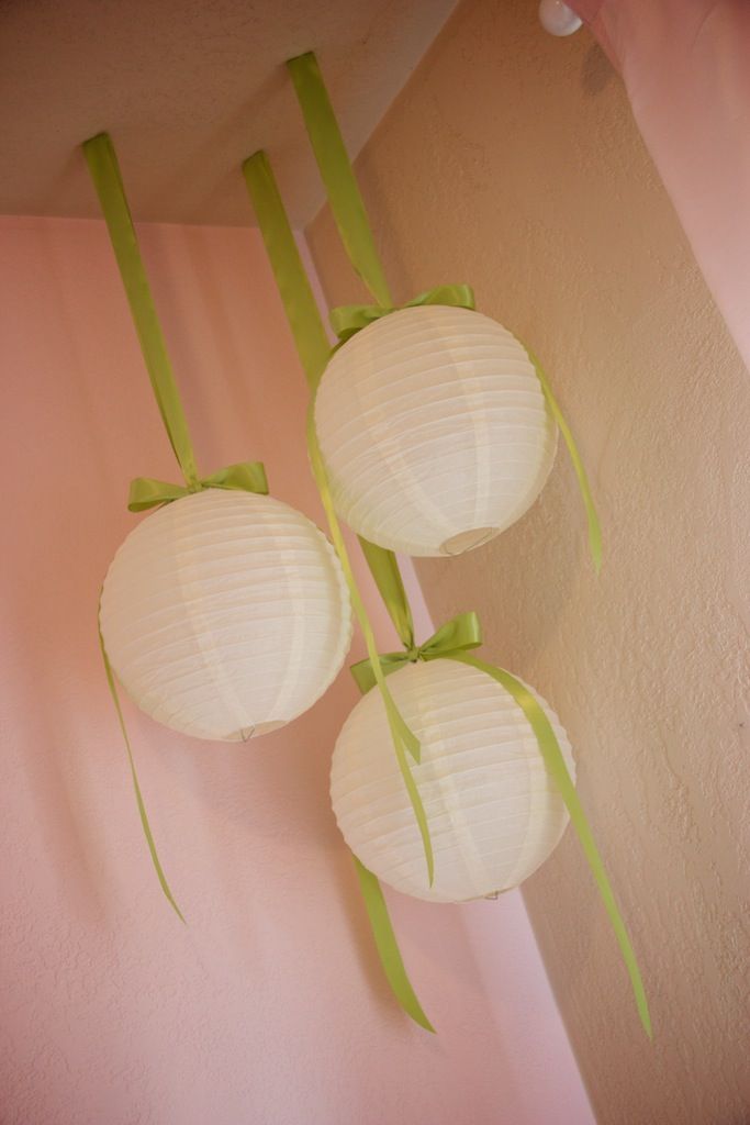 three paper lanterns hanging from the ceiling in front of a pink wall with green ribbons