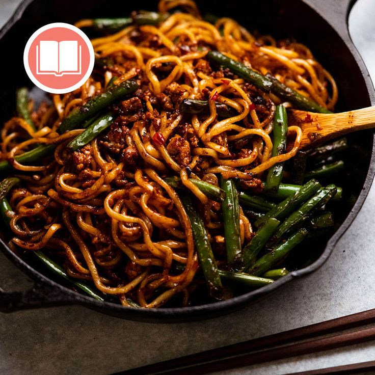 a wok filled with noodles and vegetables next to chopsticks on a table