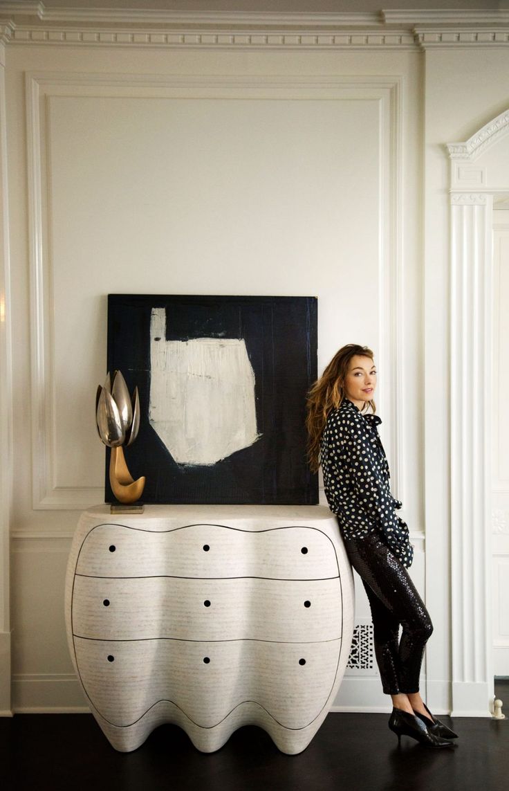 a woman sitting on top of a white table next to a painting and black chair