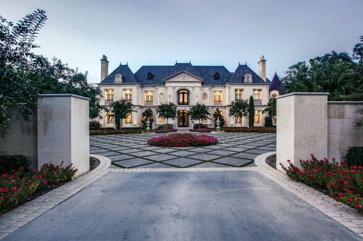 the entrance to a large home with flowers in front of it and an arched driveway