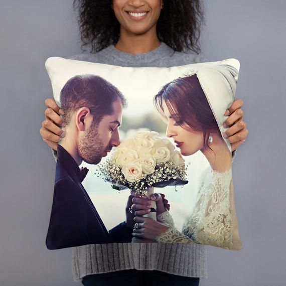 a woman holding a pillow with an image of two people on it and flowers in front of her face