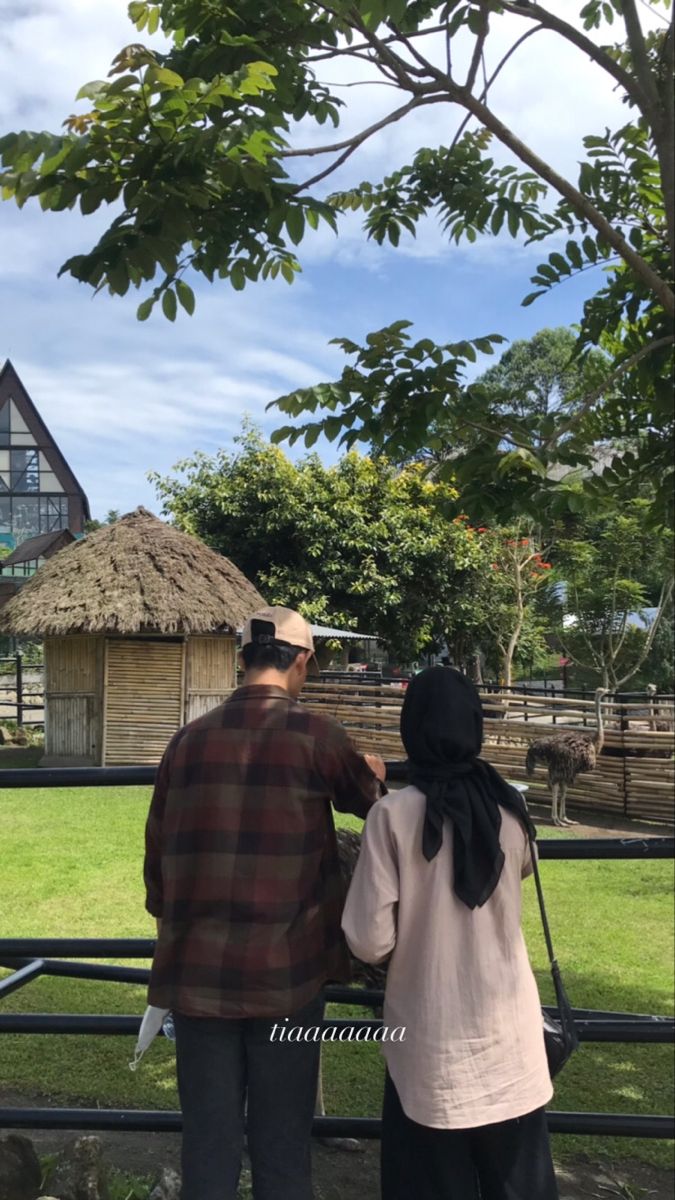 two people standing next to each other in front of a wooden fence and grass field