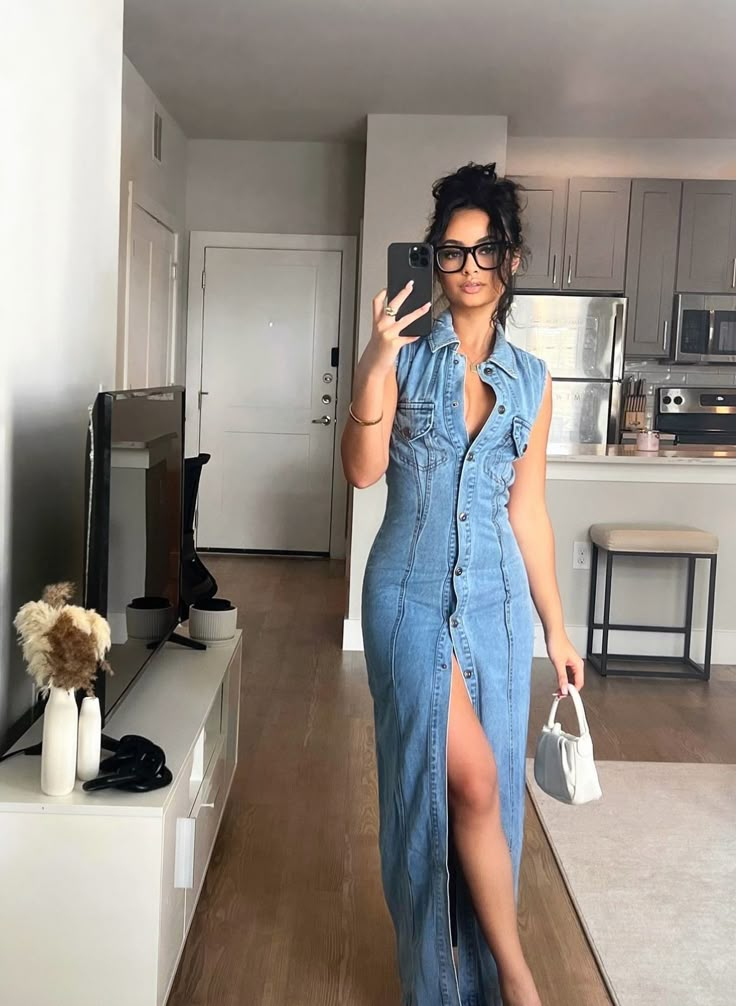 a woman taking a selfie in her living room wearing a denim dress and holding a cell phone