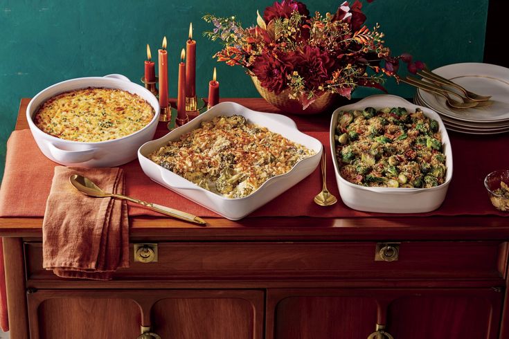 three dishes of food on a table with candles