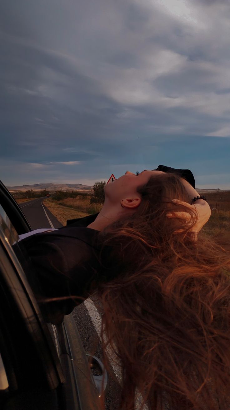 a woman with long hair leaning out the window of a car looking up into the sky