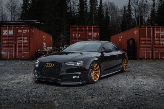 a black car with gold rims parked in front of shipping containers