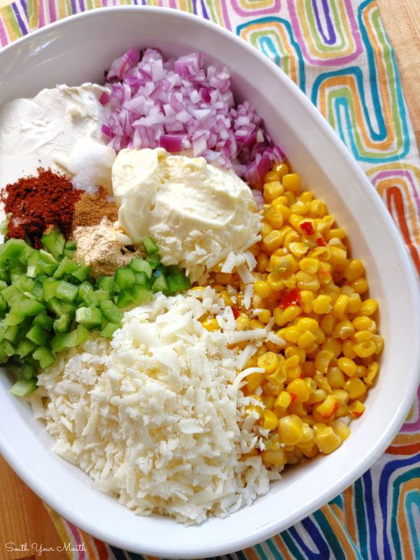 a white bowl filled with rice, corn and other vegetables on top of a colorful table cloth