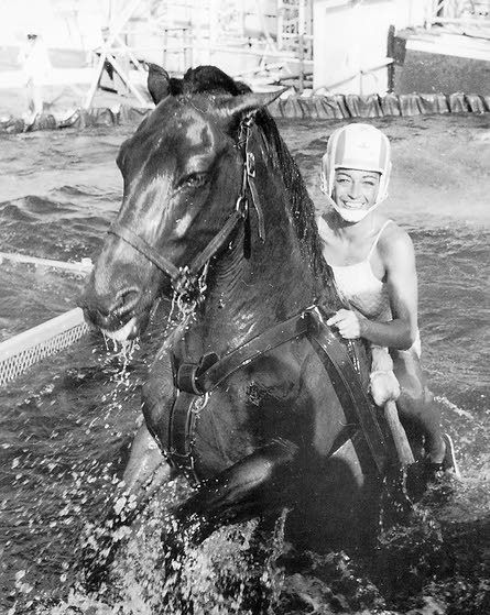 a woman riding on the back of a horse through water