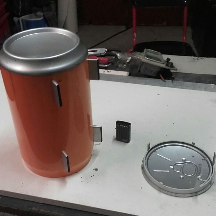 an orange trash can sitting on top of a table next to a metal object with a hole in it