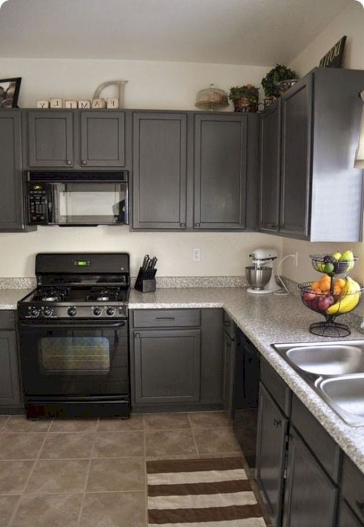 a kitchen with gray cabinets and white counter tops, black appliances and stainless steel sink