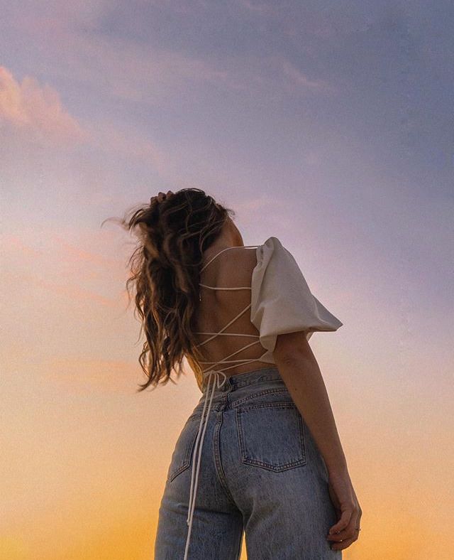 a woman standing on top of a beach next to the ocean with her back to the camera