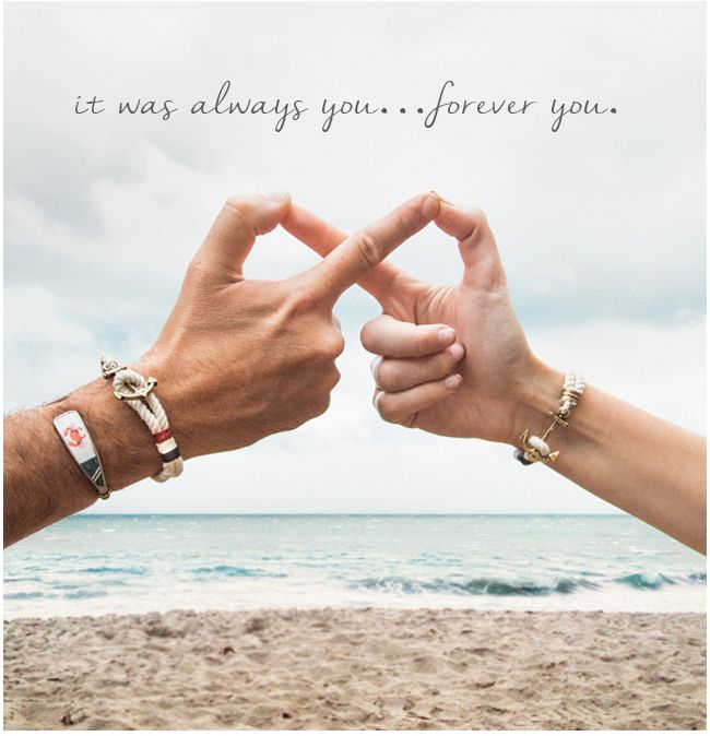 two people making a heart shape with their hands on the beach near the ocean and sky