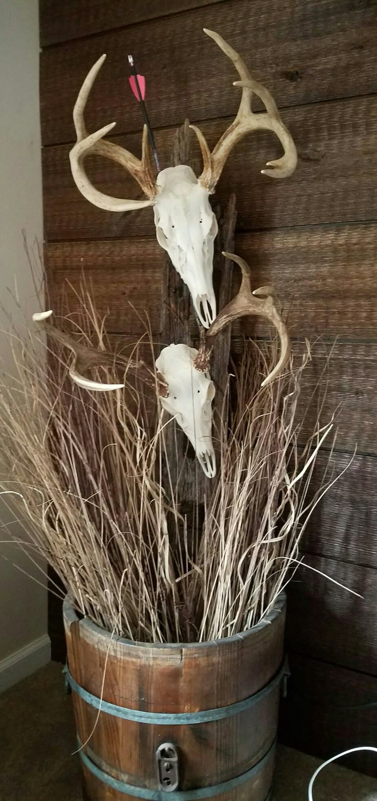 two deer heads mounted to the side of a wooden barrel with dry grass in it