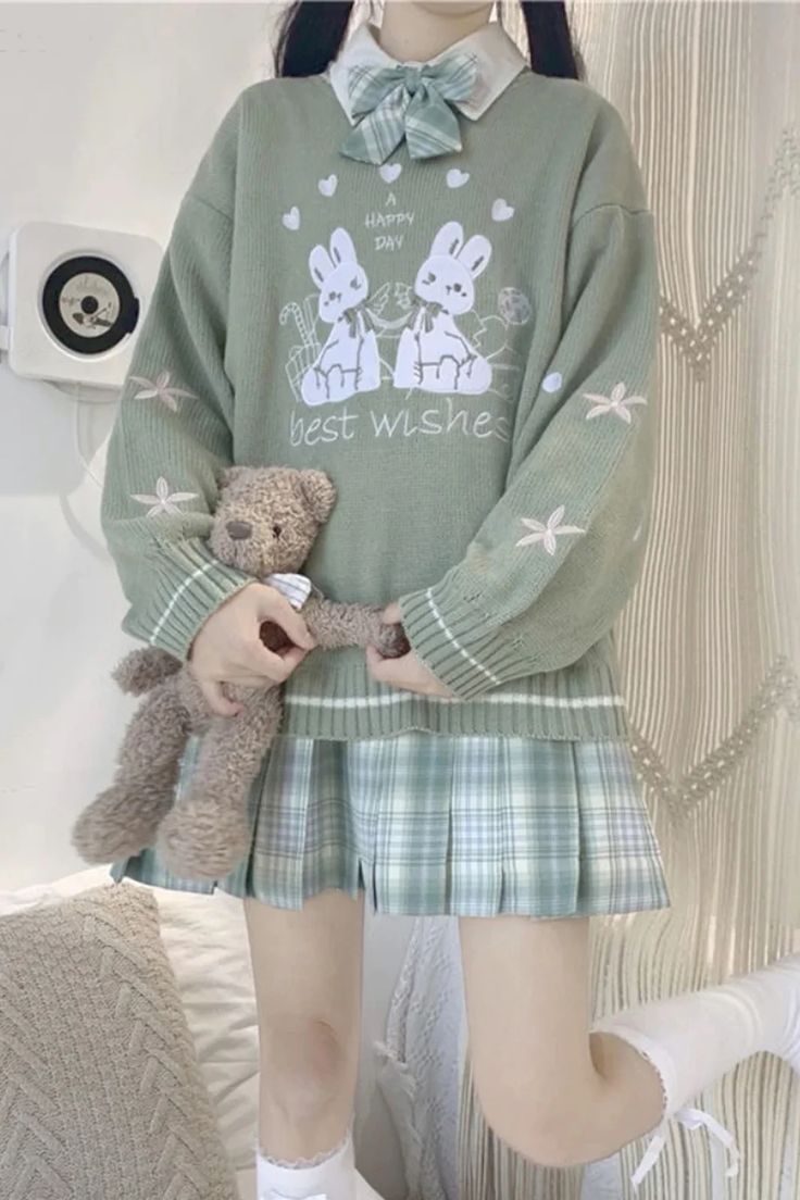 a girl in a green sweater holding a teddy bear