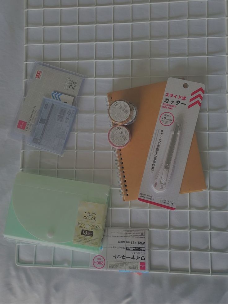 various office supplies laid out on top of a white tile floor, including a watch and notebook