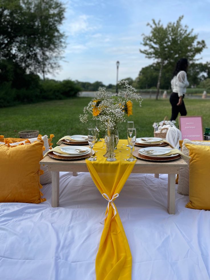 the table is set with yellow linens and place settings for an outdoor dinner party