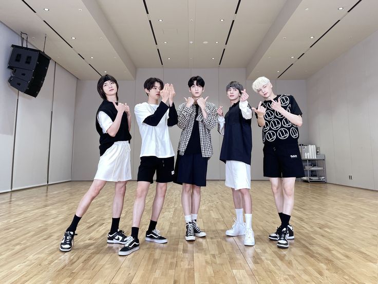 four young men standing in an empty room with one holding his hands up to the side