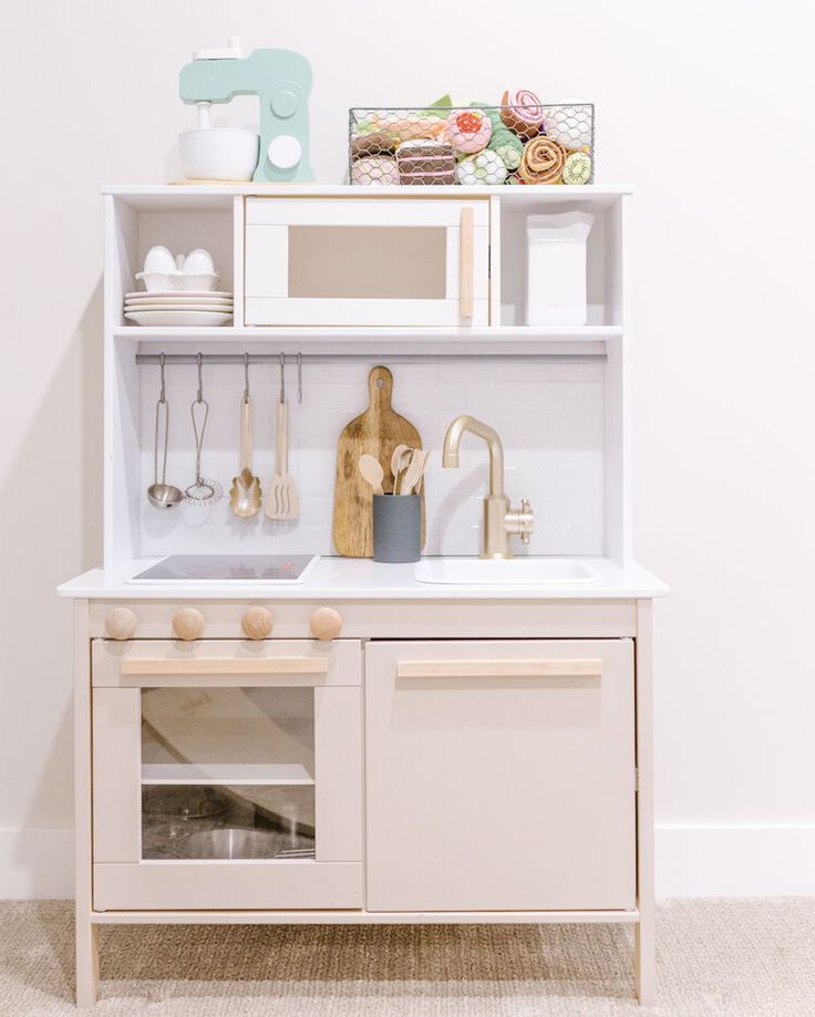 a white kitchen with an oven, sink and shelves above the stove top is filled with cooking utensils