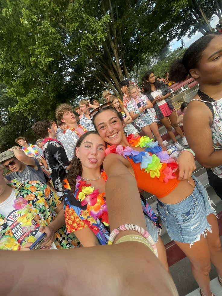 two women in colorful outfits standing next to each other and pointing at the camera with people behind them