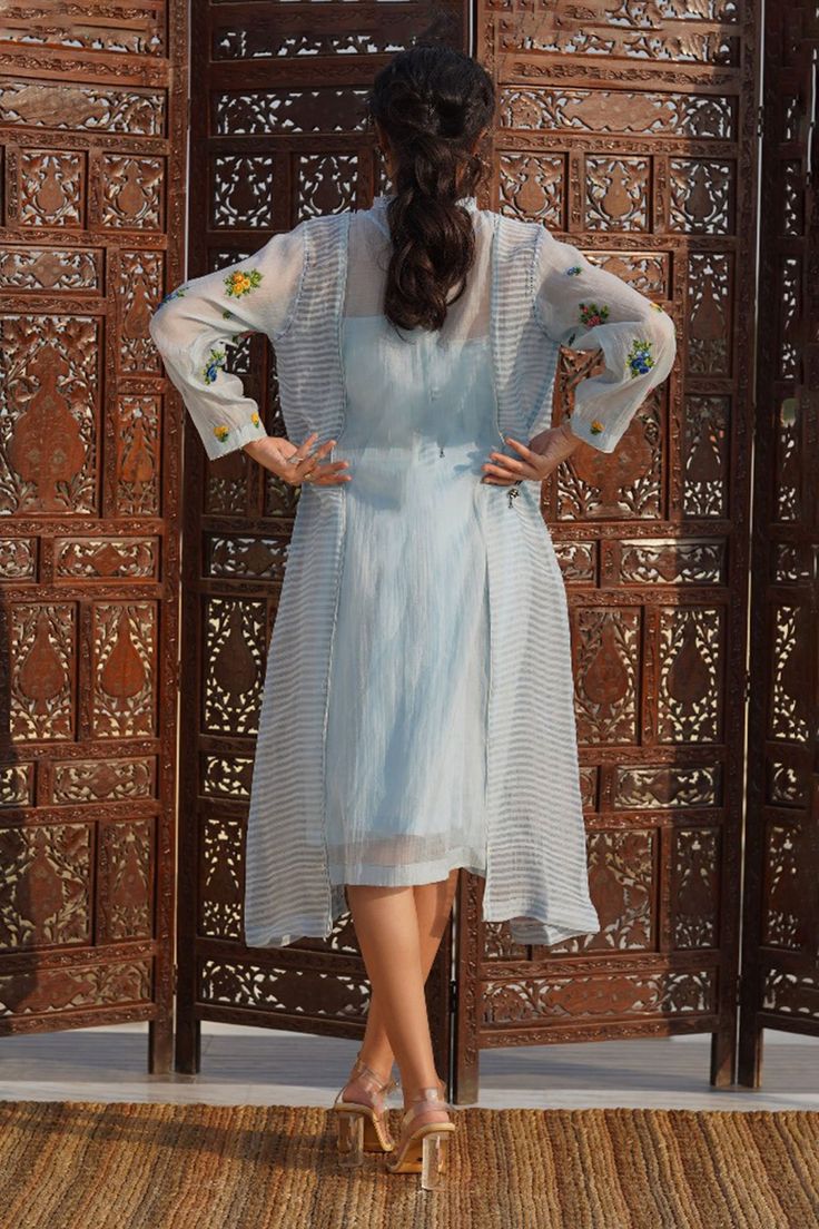 Powder blue dress with kantha embroidery and floral handwork on the sleeves. Comes with a slip. 
Component: 2
Embroidered
Neckline: High Neck
Sleeve Length: Three Quarter
Fabric: Cotton Silk
Color: Blue
Front button placket
Ruffle neckline
Asymmetric hem - Aza Fashions Fitted Cotton Silk Long Sleeve Dress, Fitted Long Sleeve Dress In Cotton Silk, Fitted Long Sleeve Cotton Silk Dress, Eid Dress With Resham Embroidery And Front Open Design, Eid Front Open Dress With Resham Embroidery, Eid Dresses With Resham Embroidery And Front Open, Eid Resham Embroidery Front Open Dress, Long Sleeve Cotton Silk Dress With Intricate Embroidery, Summer Straight Kurta Set With Embroidered Sleeves