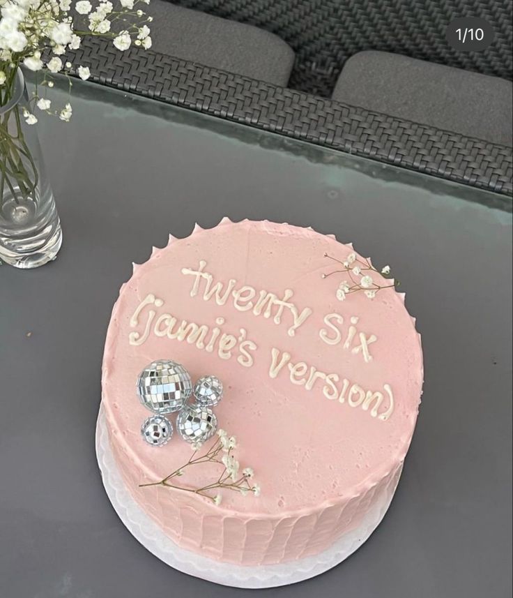 a pink cake sitting on top of a table next to a vase filled with flowers