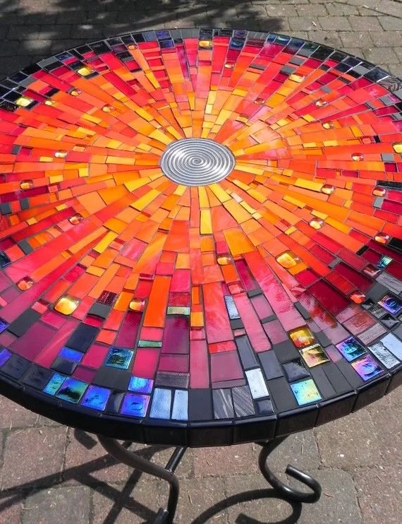 a table made out of many different colored glass tiles on top of metal legs with a circular design in the center