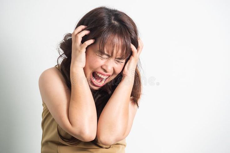 a woman is holding her head with both hands and screaming at something while standing against a white background