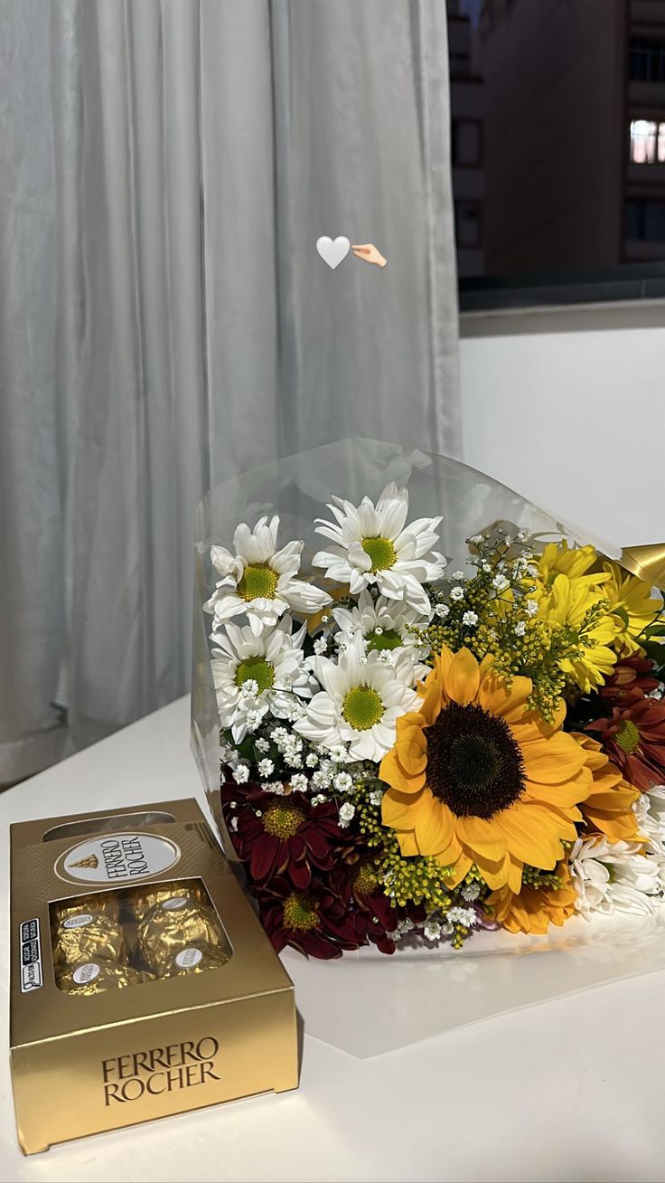 a bouquet of sunflowers, daisies and other flowers next to a chocolate box