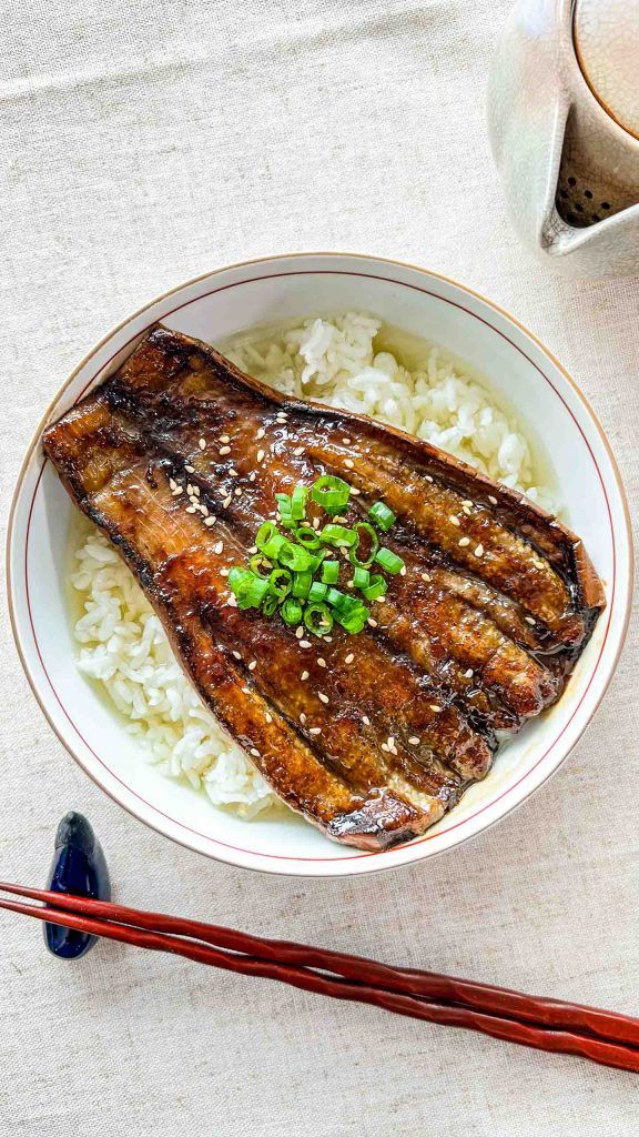 a bowl filled with meat and rice next to chopsticks on top of a table