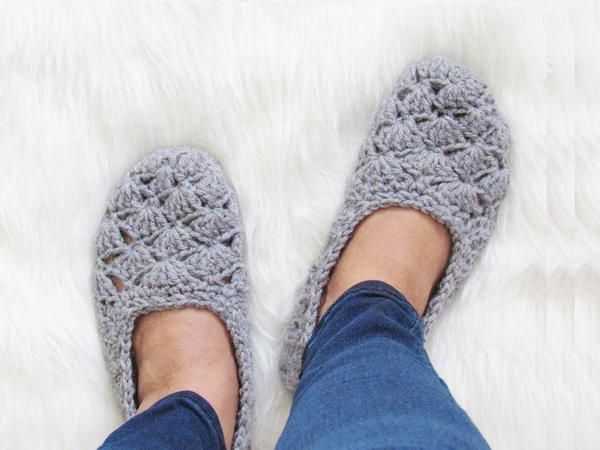 a woman's feet wearing crochet slippers on top of a fluffy white rug