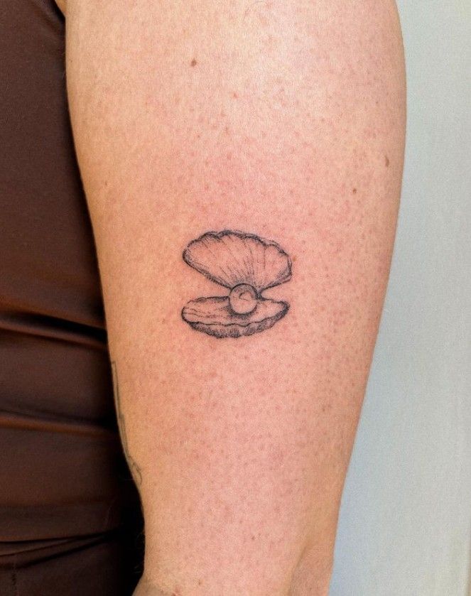 a woman's arm with a small tattoo of a seashell on the left shoulder