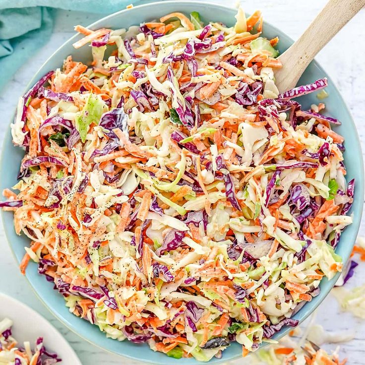 a bowl full of coleslaw and carrots with a wooden spoon in it