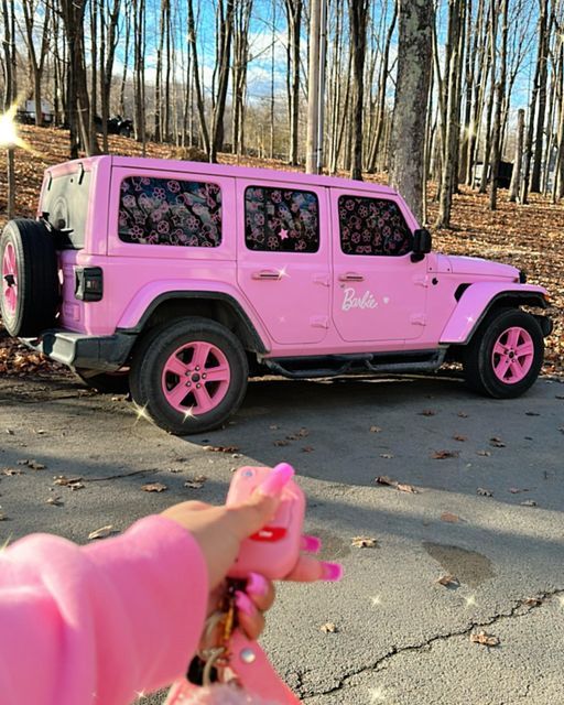 a pink jeep parked on the side of a road with trees in the back ground