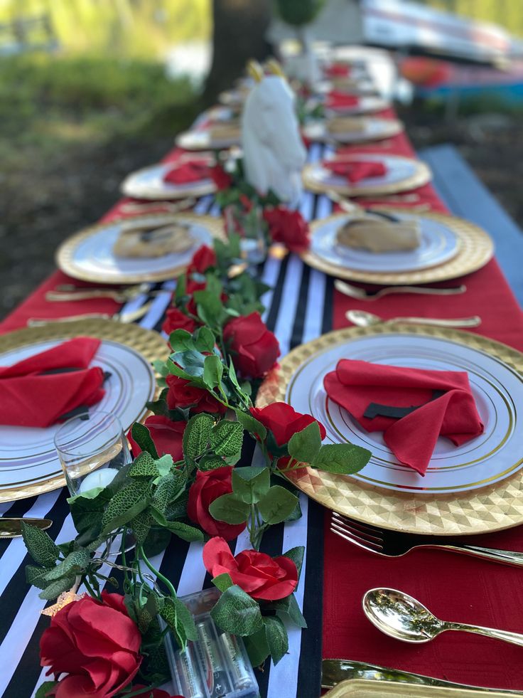 the table is set with red roses and gold place settings for an elegant dinner party