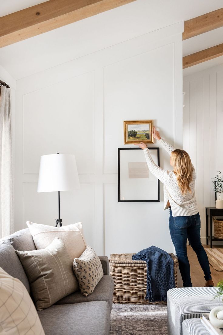 a woman is hanging pictures on the wall in her living room while she stands up