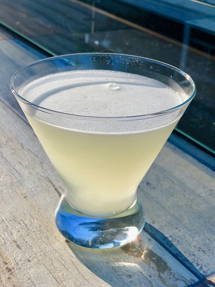 a glass filled with liquid sitting on top of a wooden table next to a window