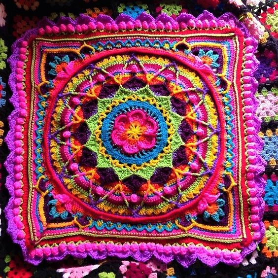 a crocheted square that has been placed on top of a blanket with multicolored yarns