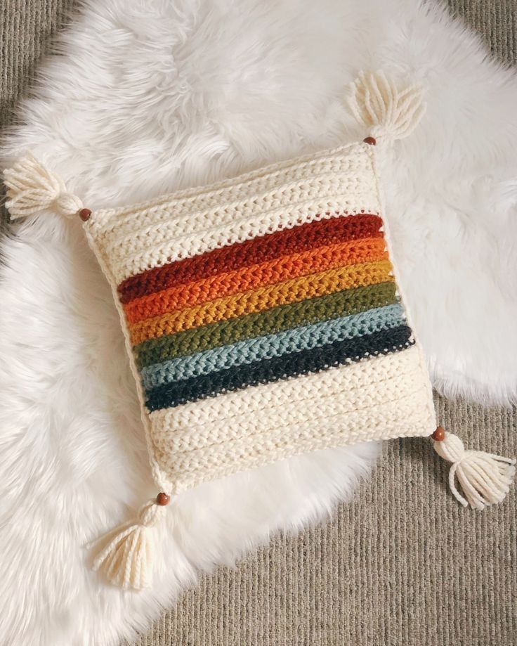 a multicolored crocheted pillow on a white fur rug with tassels