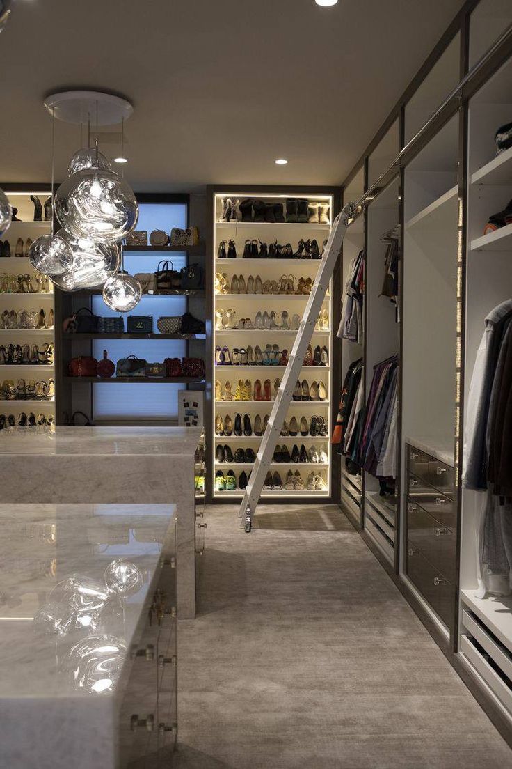 a walk in closet with lots of shoes on the shelves and lights hanging from the ceiling