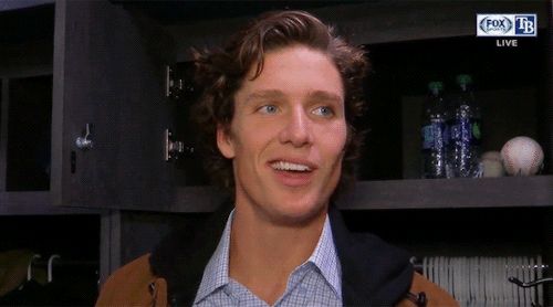 a man with curly hair wearing a brown jacket and blue shirt is smiling at the camera