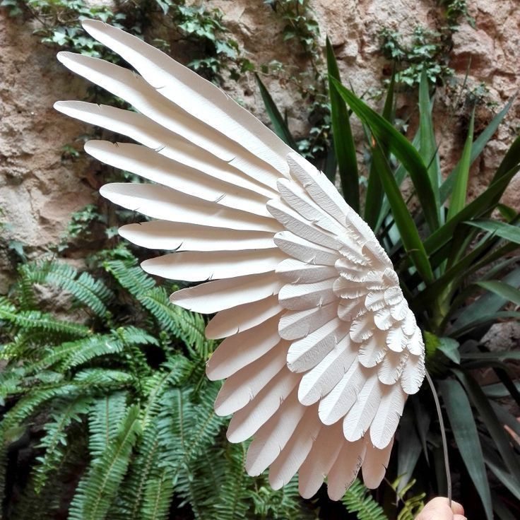 a paper sculpture of an angel wings in front of some plants and rocks with green leaves