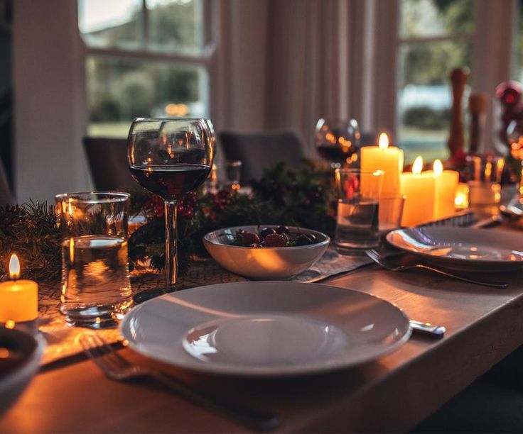 a table set for christmas with candles, plates and wine glasses on the dining room table