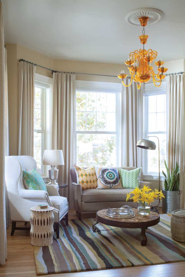 a living room filled with furniture and a chandelier hanging from the ceiling in front of two windows