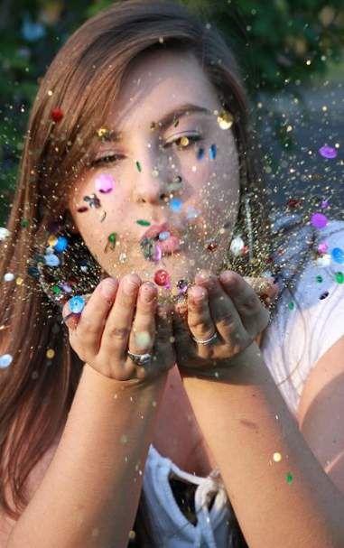 a girl is blowing confetti on her face